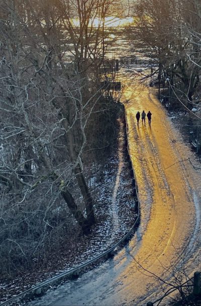 Three persons walking on a road in sunset